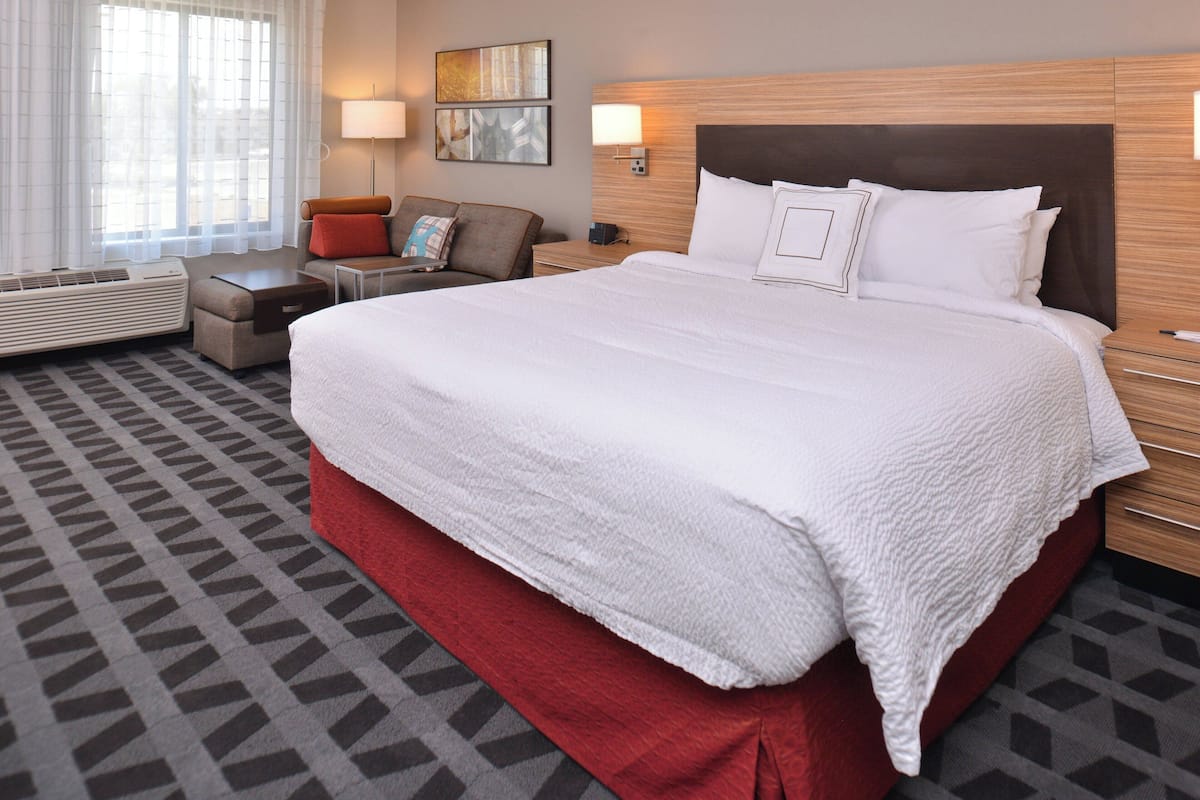 A hotel room with a large bed, a sofa, a desk, and a window with curtains.