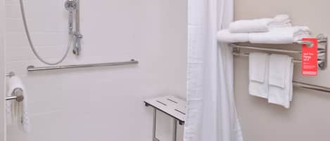 A bathroom with a shower, a towel rack with folded towels, and a small table.