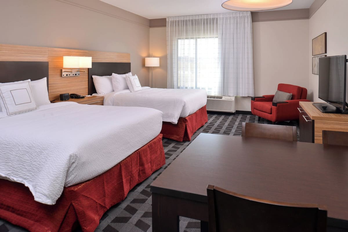 A hotel room with two beds, a desk, a chair, a television, and a window with curtains.