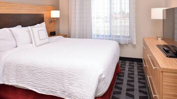 A hotel room with a large bed, a wooden headboard, a bedside table with a lamp, a TV, and a patterned rug.