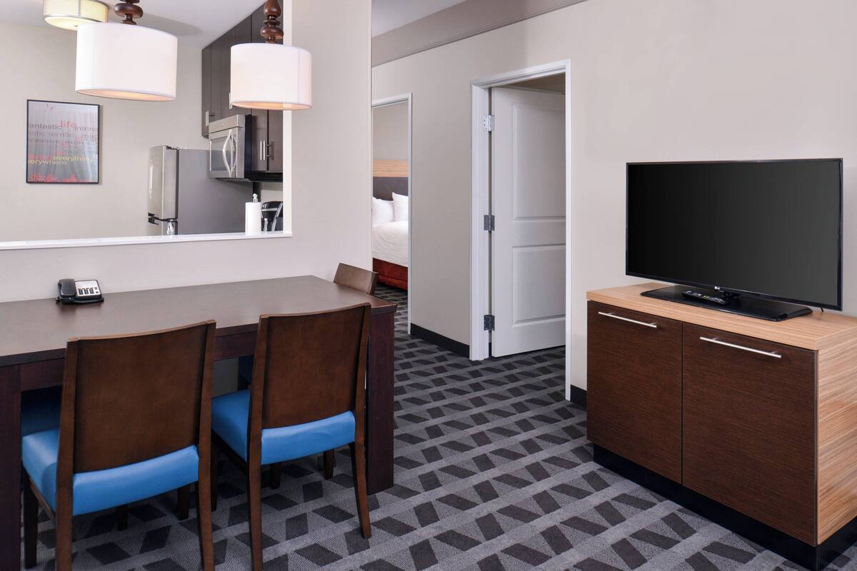 A hotel room with a dining area, a TV, and a bed.