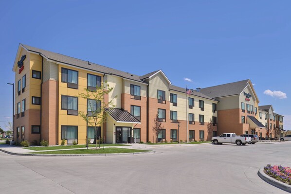 A multi-story hotel with a modern design, featuring a mix of beige and brown exterior colors, large windows, and a parking lot with a white pickup truck. - TownePlace Suites by Marriott Gillette (Gillette)