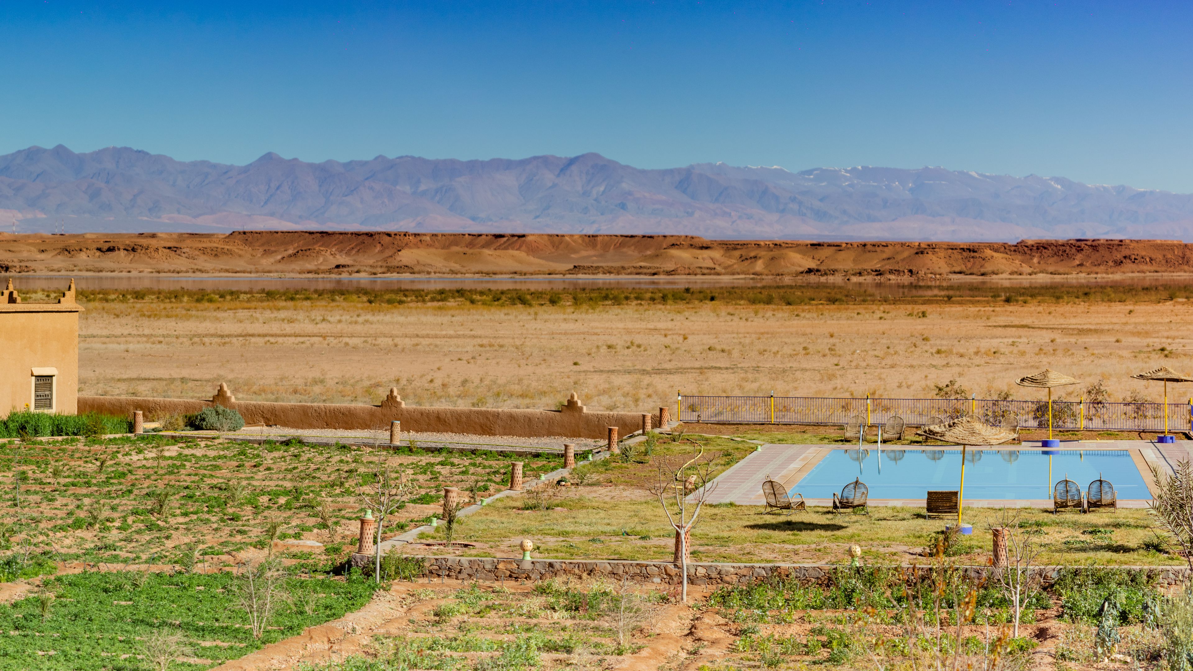 Paisaje desértico con piscina, mobiliario exterior y un pequeño edificio.