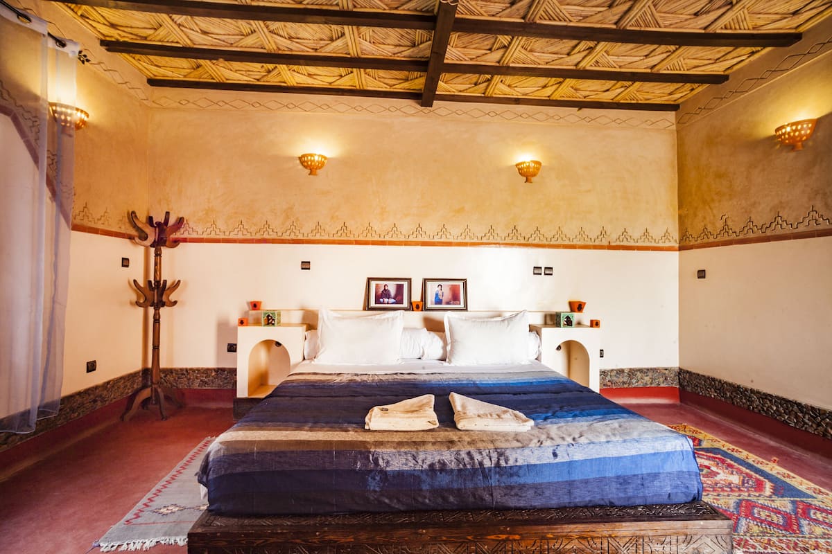 A traditional room with a bed, two wall-mounted lights, a decorative wall pattern, and a wooden floor.
