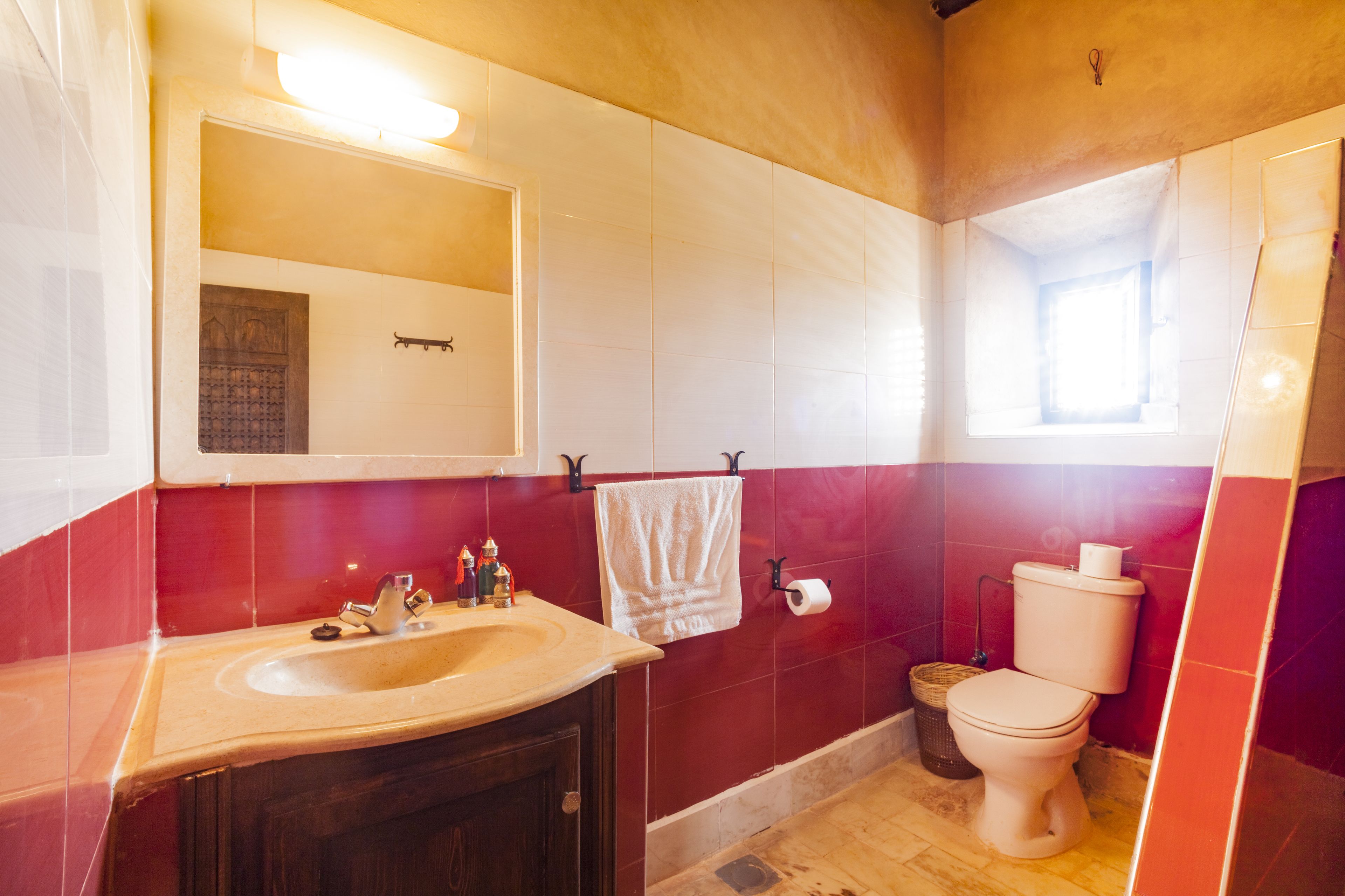 A bathroom with a sink, mirror, toilet, and red-tiled walls.