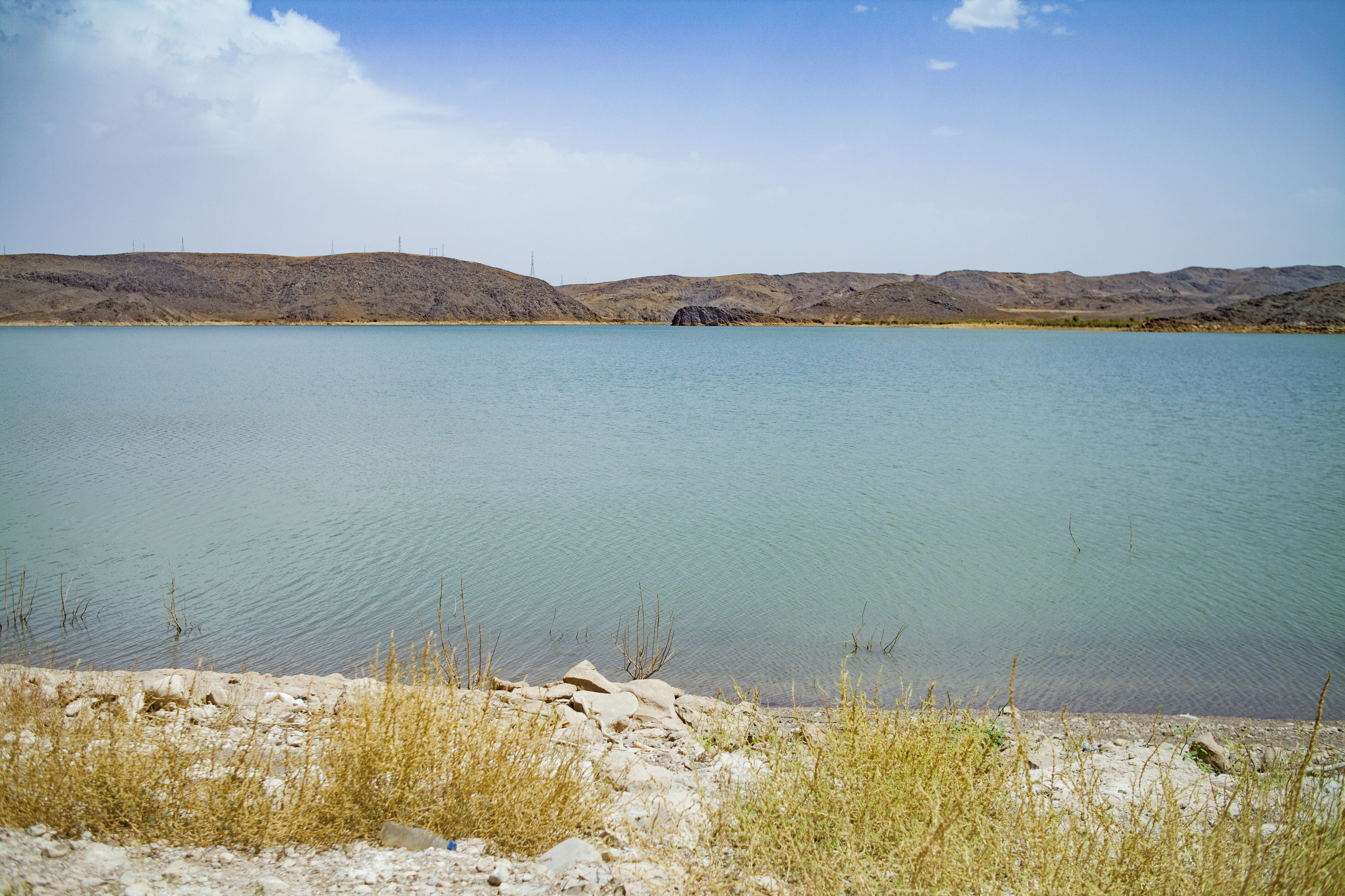A calm lake with a rocky shoreline and distant hills.