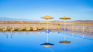 Una piscina amb dues paraigües, una tanca i un paisatge desèrtic al fons.