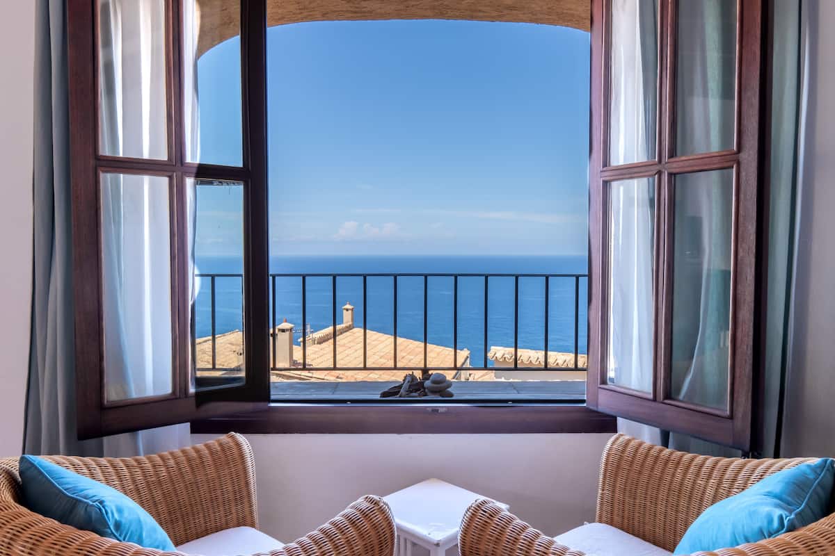 Una habitación con vista al mar a través de un ventanal con cortinas.