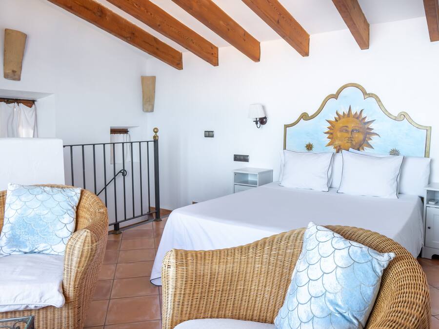 Quarto com cama, duas cadeiras de vime, mesa de cabeceira e parede com mural do sol.