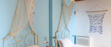 A bedroom with two beds, a wooden nightstand, a wall-mounted heater, and decorative nets on the beds.