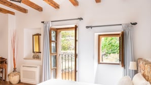A bedroom with a bed, a window, a radiator, a mirror, and a door leading to an outdoor area. - Hotel Son Borguny (Banyalbufar)