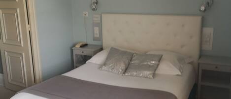 A bedroom with a large bed, a nightstand, a dresser, and a door.
