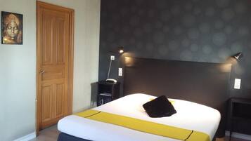A bedroom with a wooden door, a bed with a yellow accent, a headboard, and a wall with circular patterns.