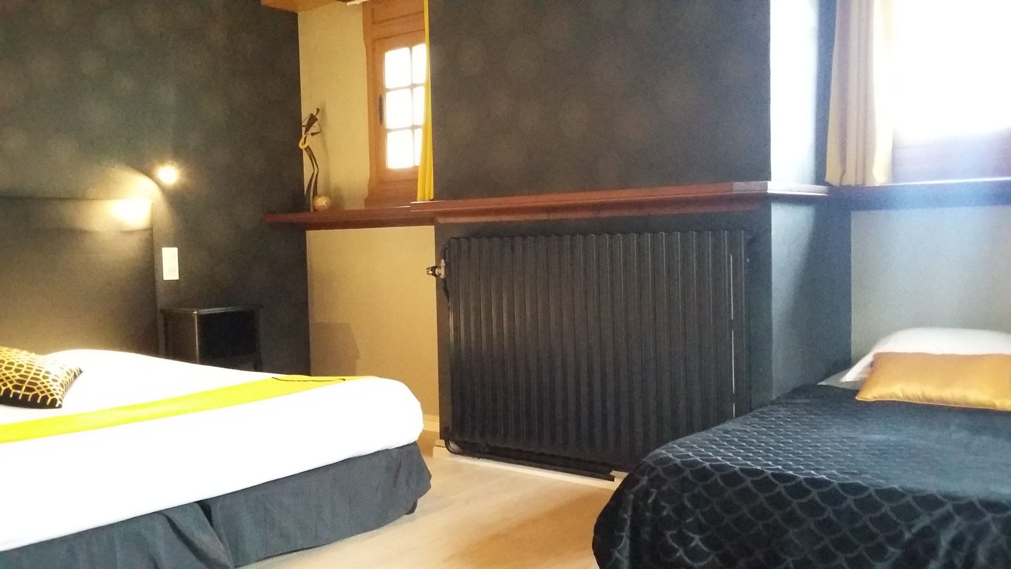 Une chambre d’hôtel avec deux lits, un radiateur, une petite table et une fenêtre avec des rideaux.