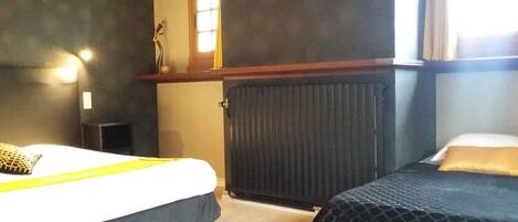 Une chambre d’hôtel avec deux lits, un radiateur, une petite table et une fenêtre avec des rideaux.