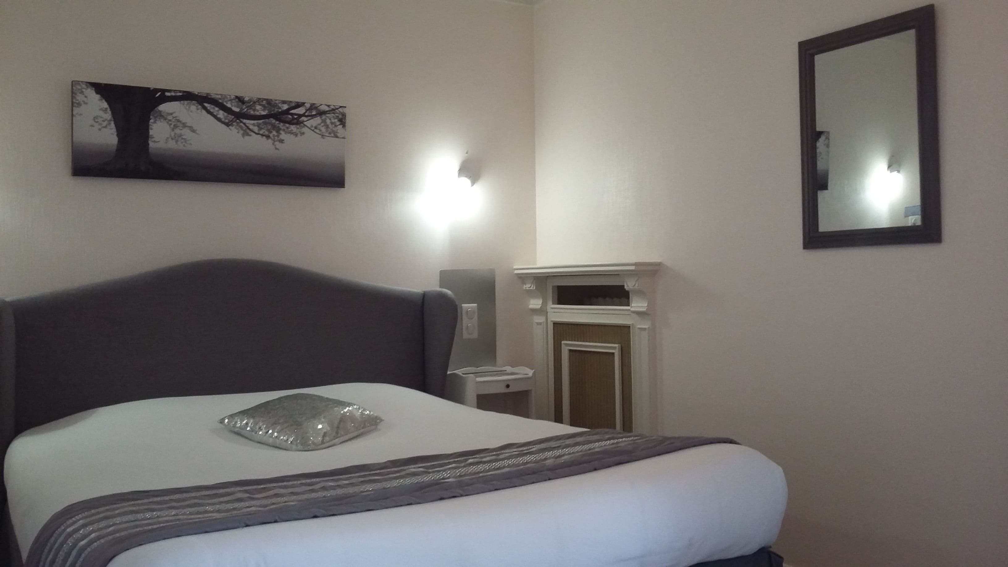 Ein Hotelzimmer mit einem Bett, einem Nachttisch, einem Spiegel und einem an der Wand hängenden Bild von einem Baum.