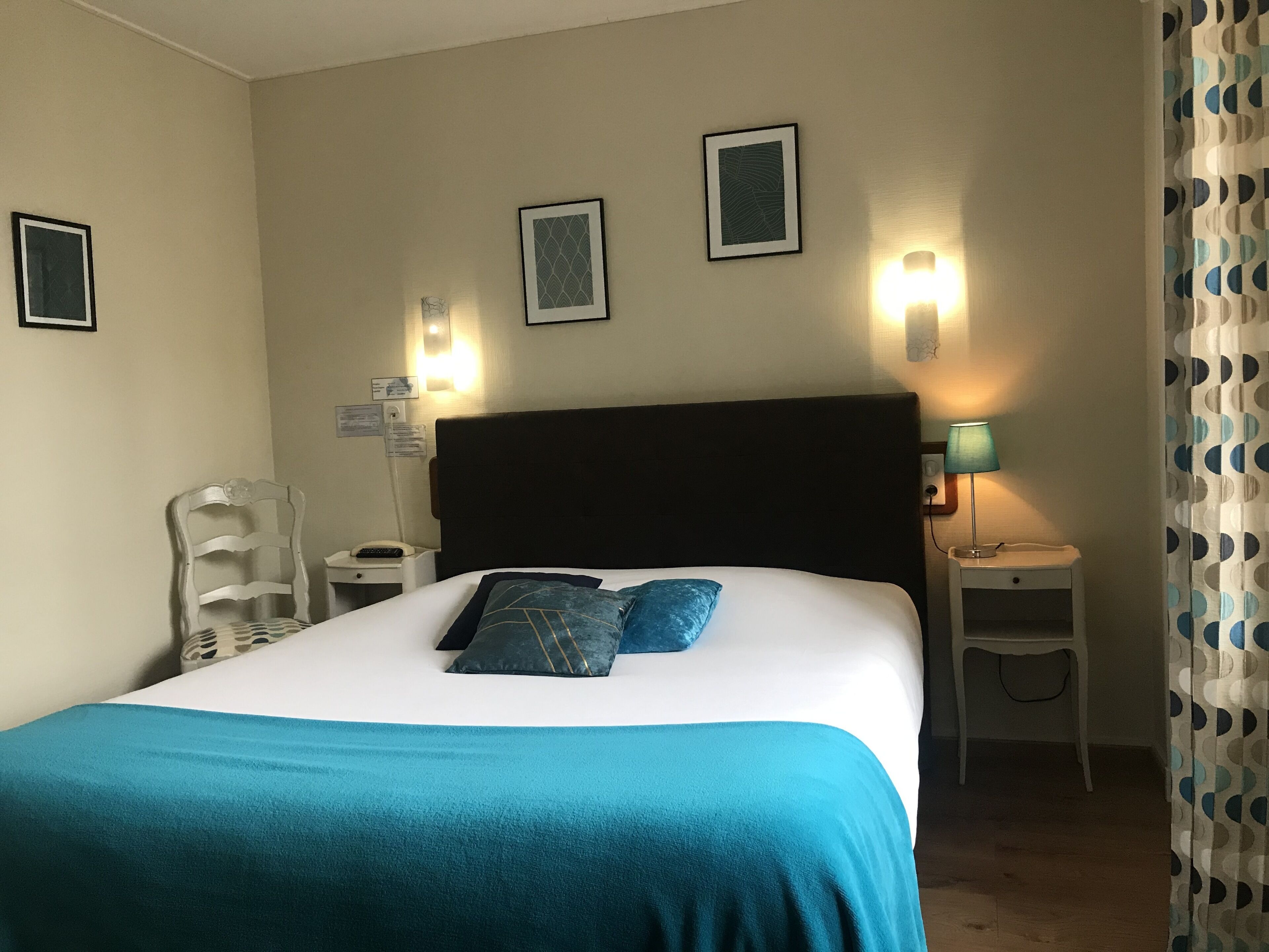 A hotel room with a bed, a chair, a nightstand, a lamp, and a curtain.