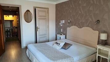 Una camera d'albergo con un letto grande, un comodino con una lampada, uno specchio a parete e una porta che dà su un corridoio.