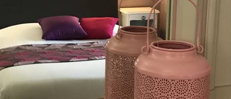 A bedroom with a bed, pillows, a nightstand, and two pink lanterns on a wooden table.