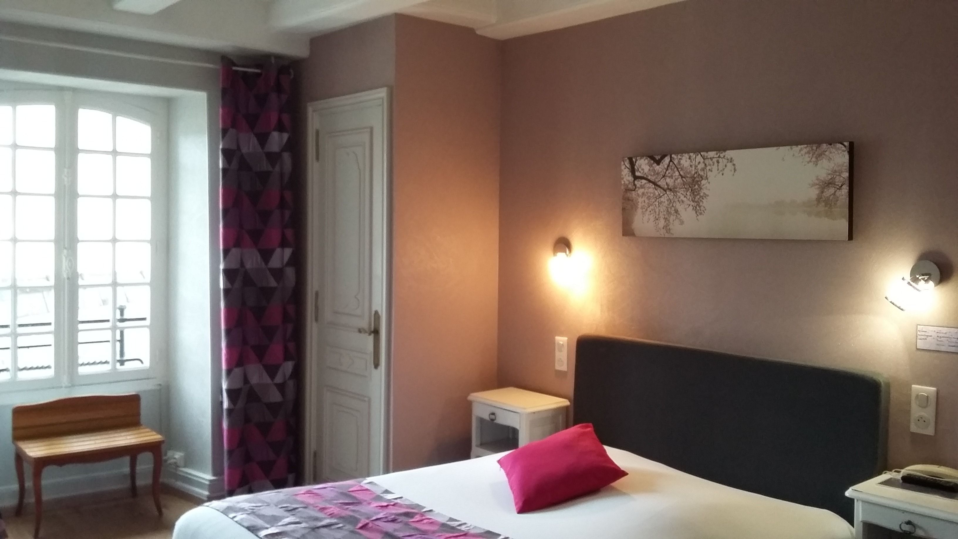 Ein Hotelzimmer mit Bett, Sitzbank, Tür und Wandleuchte.