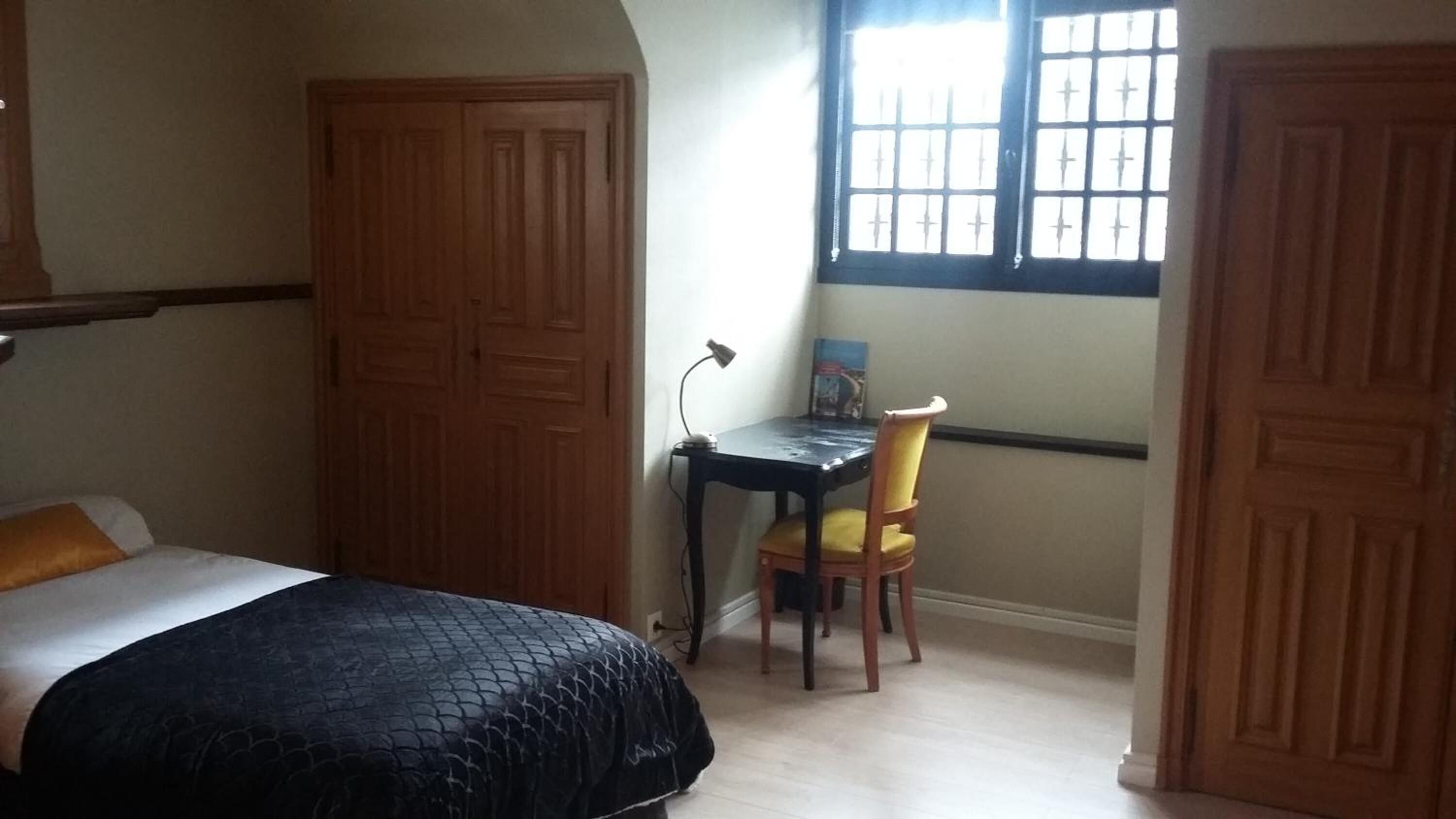 A bedroom with a bed, a desk, a chair, and a window.