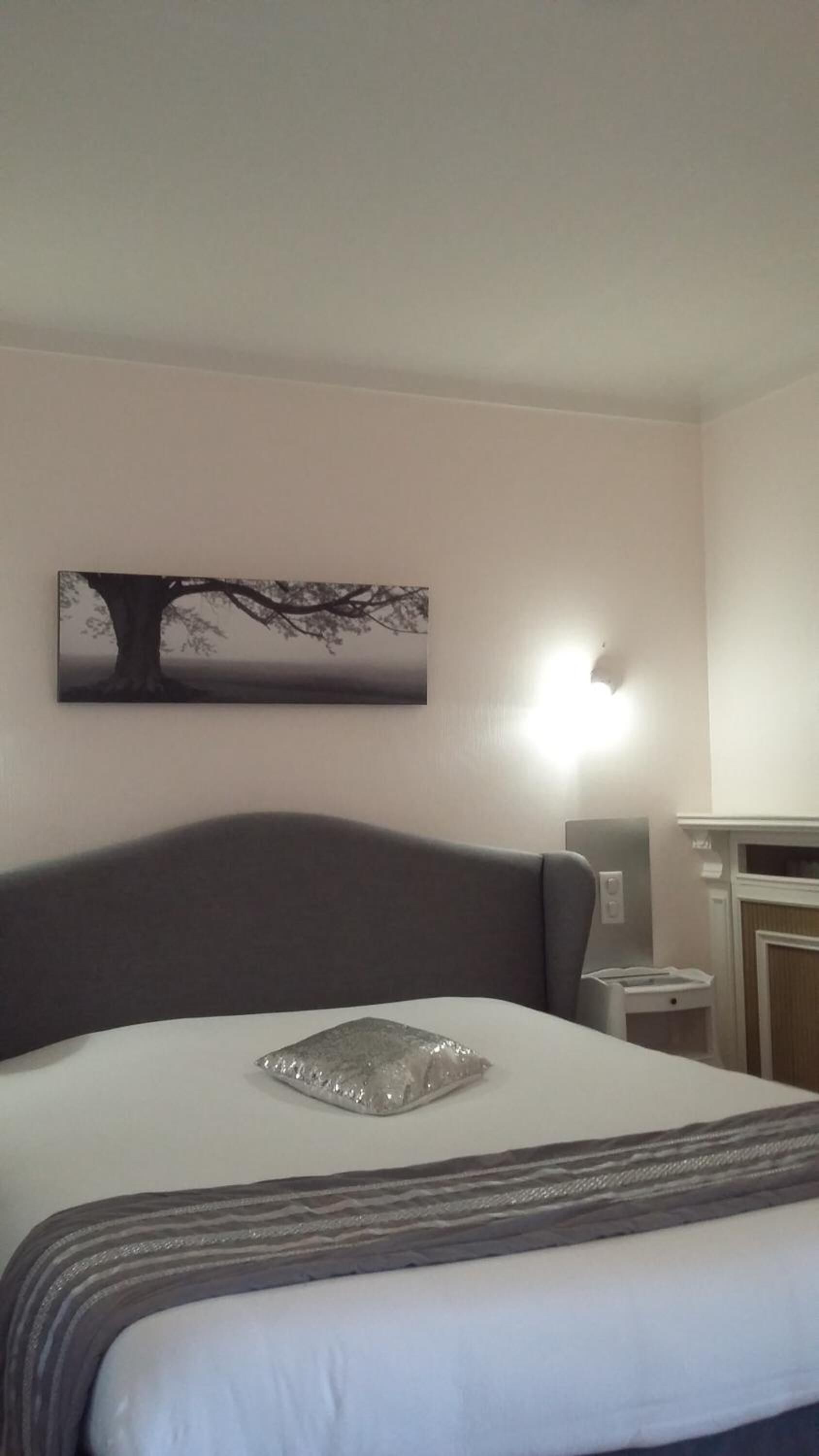 Een hotelkamer met een bed, een nachtkastje, een lamp en een schilderij van een boom.