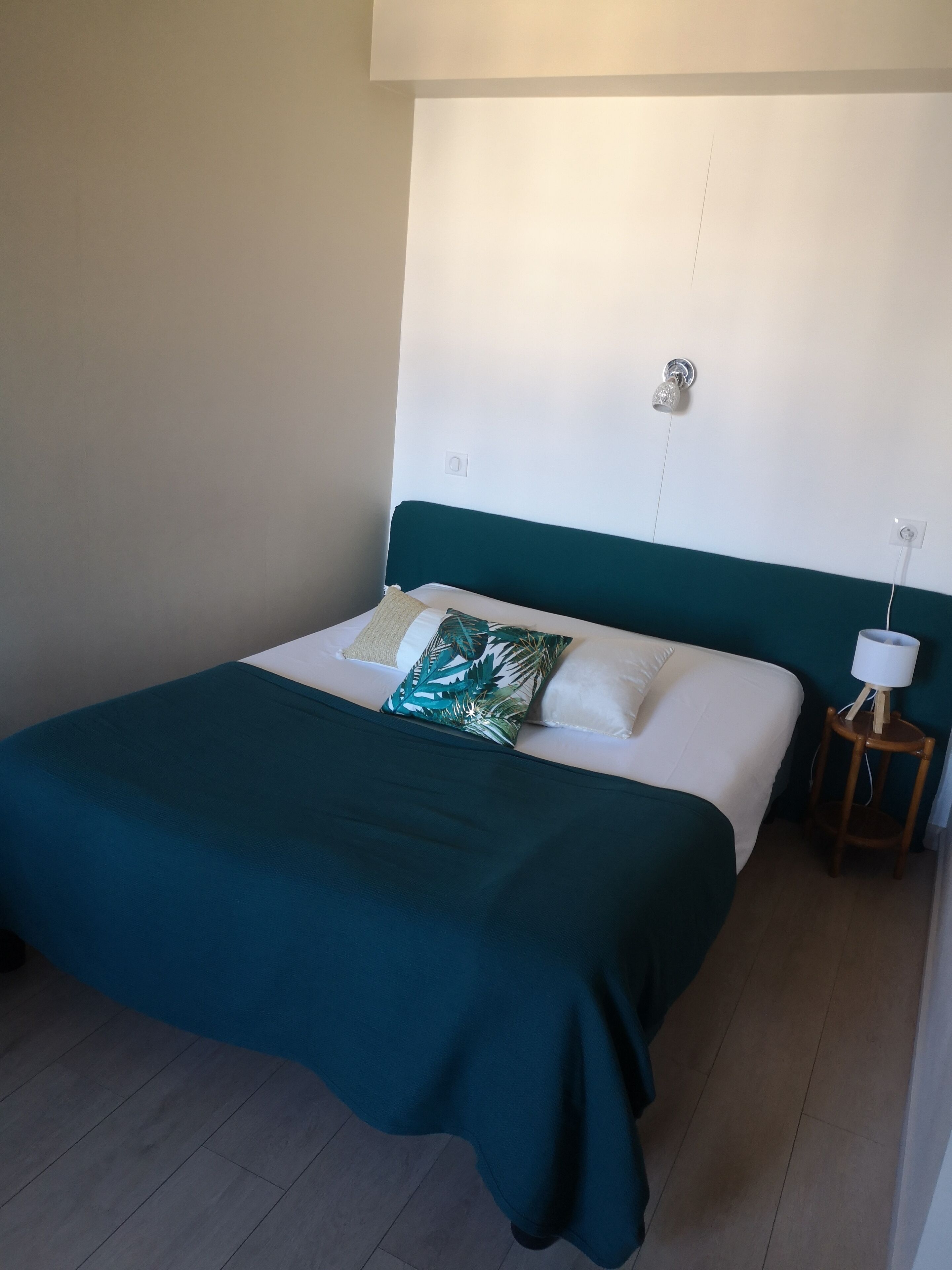 A neatly made bed with a teal headboard, white bedding, and a single green and white patterned pillow.