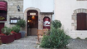 A hotel entrance with a red door, a bench outside, and stone walls. - Hôtel Les Deux Magots (La Roche-Bernard)