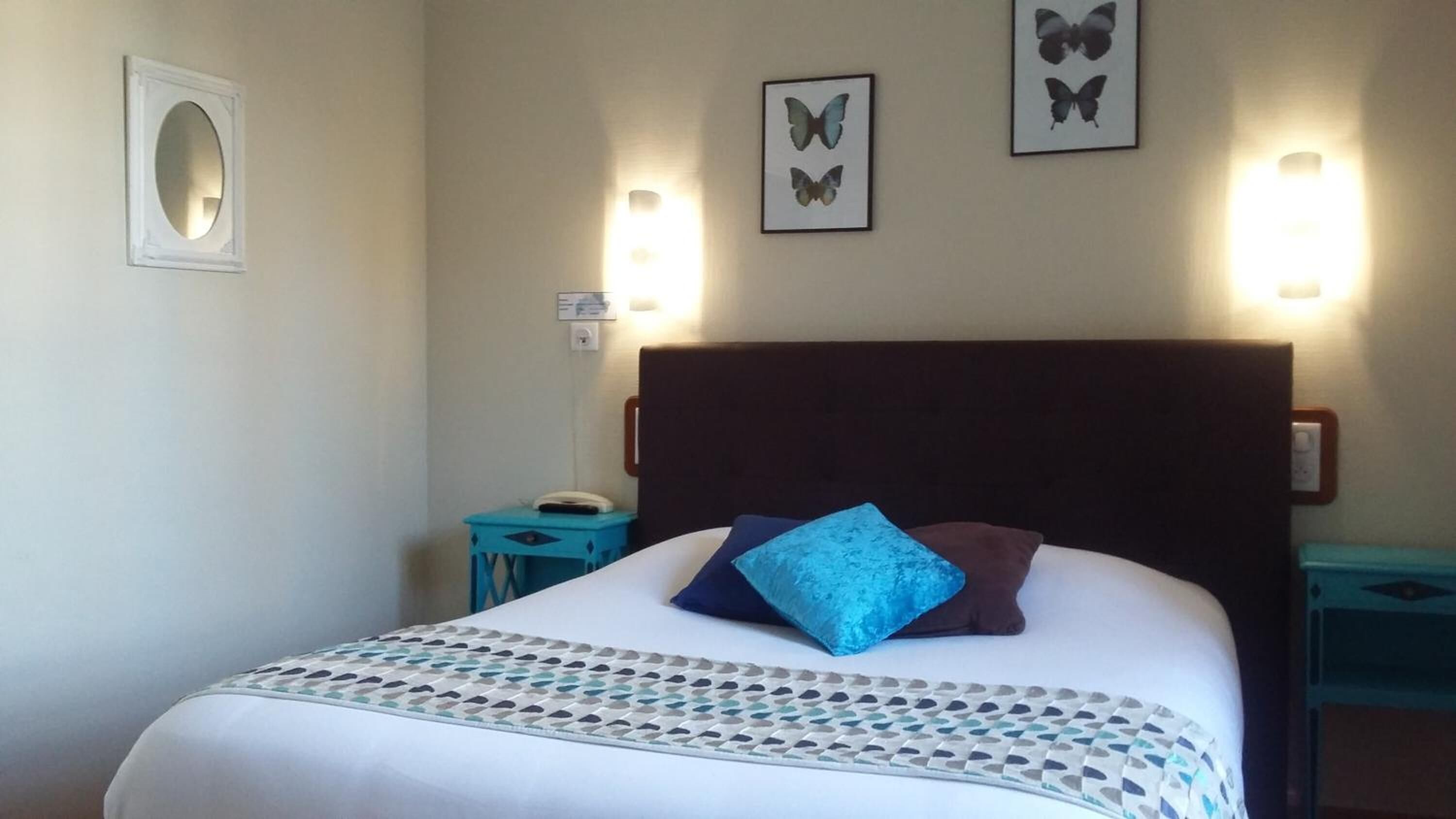 Une chambre d’hôtel avec un lit, deux tables de chevet, une lampe fixée au mur et des décorations murales représentant des papillons.