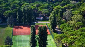 Luftaufnahme eines Tennisplatzes, umgeben von dichtem Grün und einigen Gebäuden.