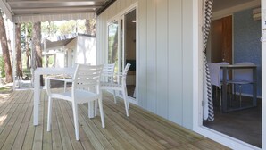 Ein überdachter Außenbereich mit Holzterrasse, weißen Plastikstühlen und einem Tisch.