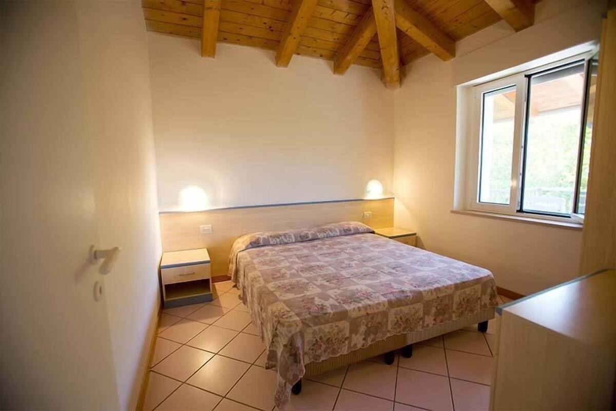 Une chambre à coucher avec un lit, des lampes de chevet, une fenêtre et un plafond en bois.