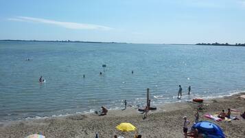Ein Strand mit badenden und sonnenden Personen. Sonnenschirme und Liegen stehen im Sand.