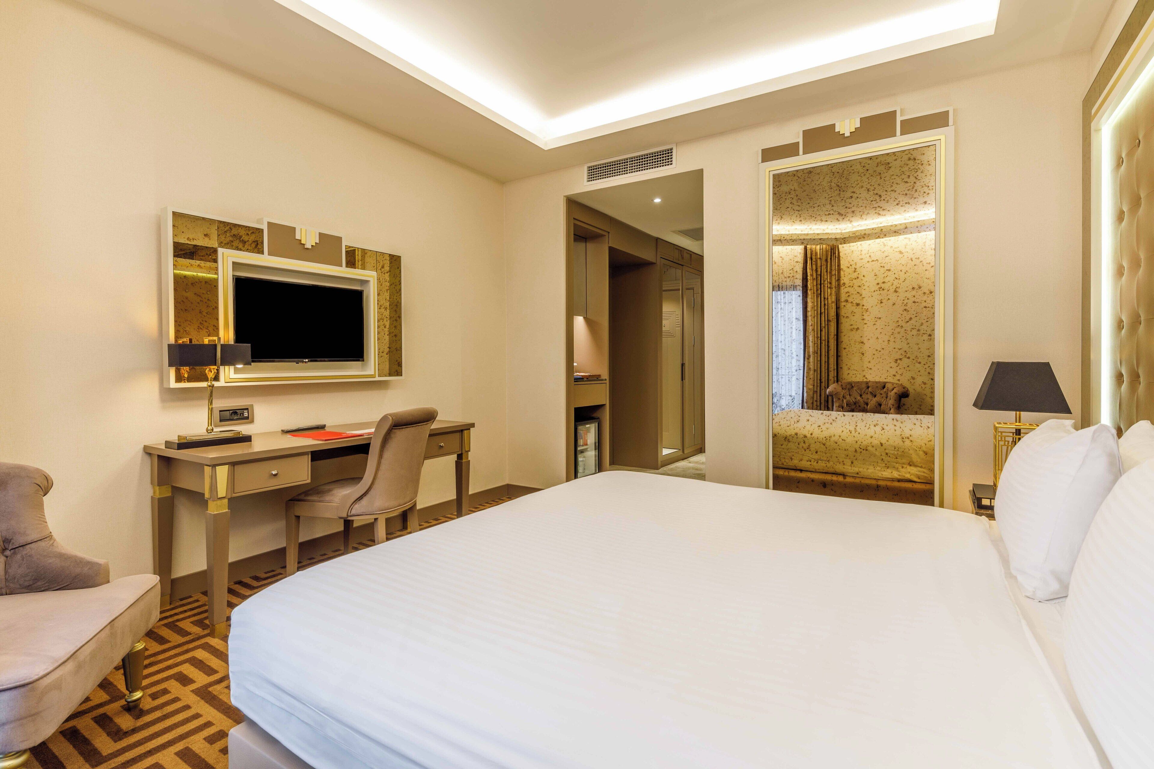 Habitación de hotel con una cama grande, un escritorio con silla, televisión y espejo.