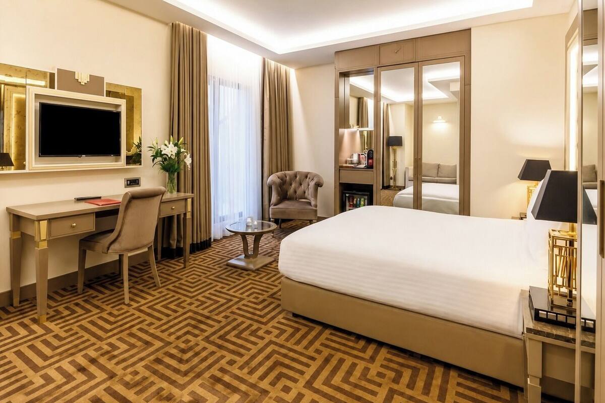 Een hotelkamer met een bed, een bureau, een stoel, een televisie, een spiegel en een raam met gordijnen.
