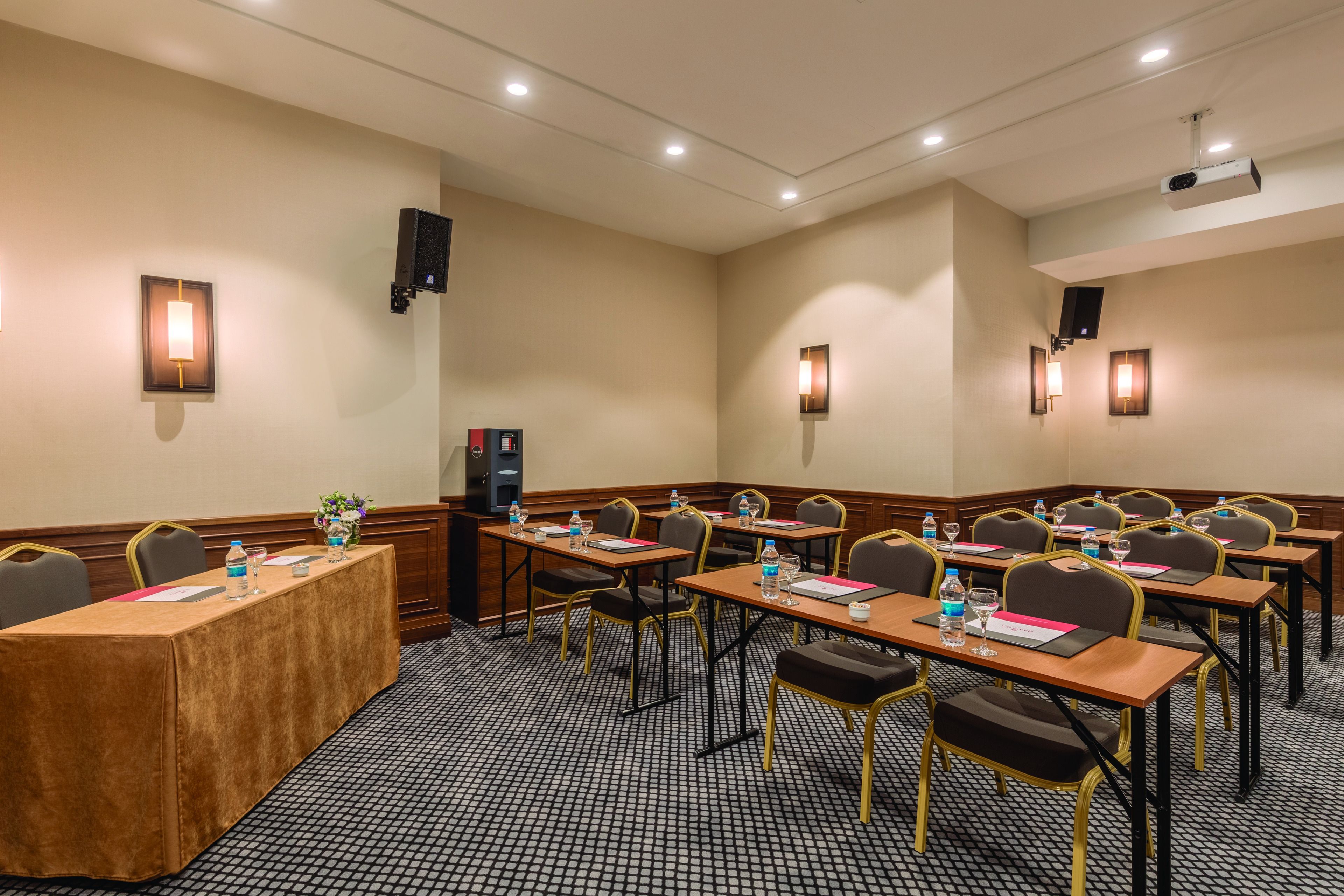 Sala de conferências com mesas, cadeiras e um projetor.