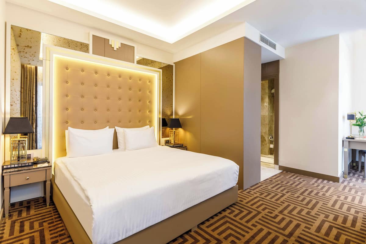 Een hotelkamer met een groot bed, een nachtkastje, een lamp, een spiegel en een douche.