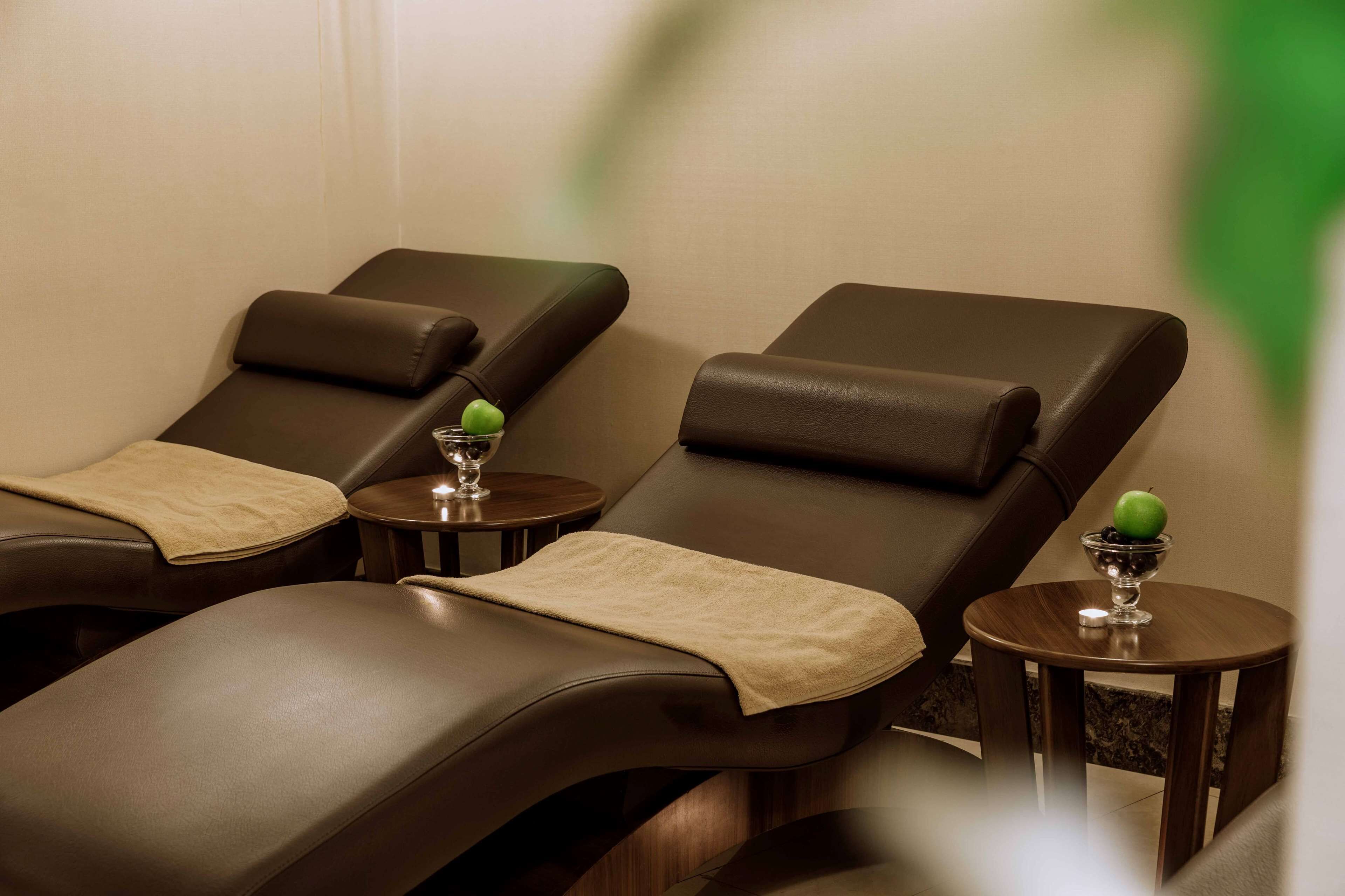 A massage therapy room with three reclining chairs, each with a towel and a small table with a glass and an apple.