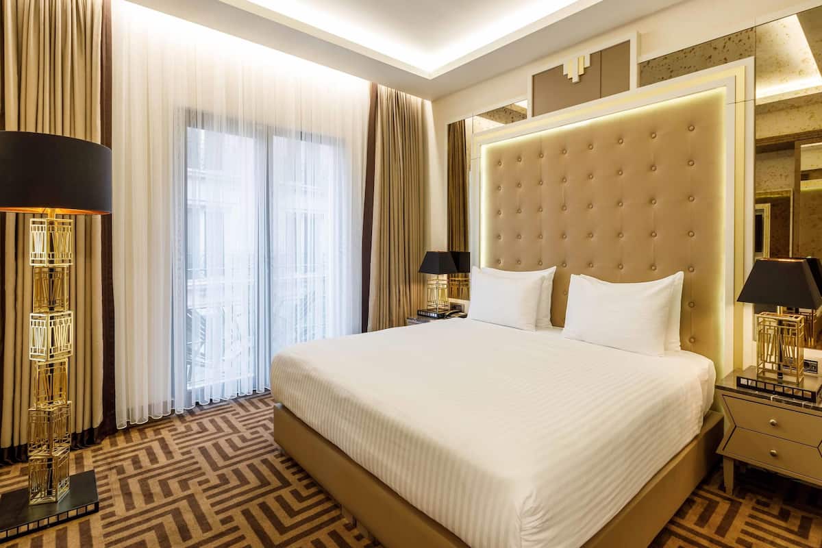 Een hotelkamer met een groot bed, een nachtkastje, een lamp en een raam met gordijnen.