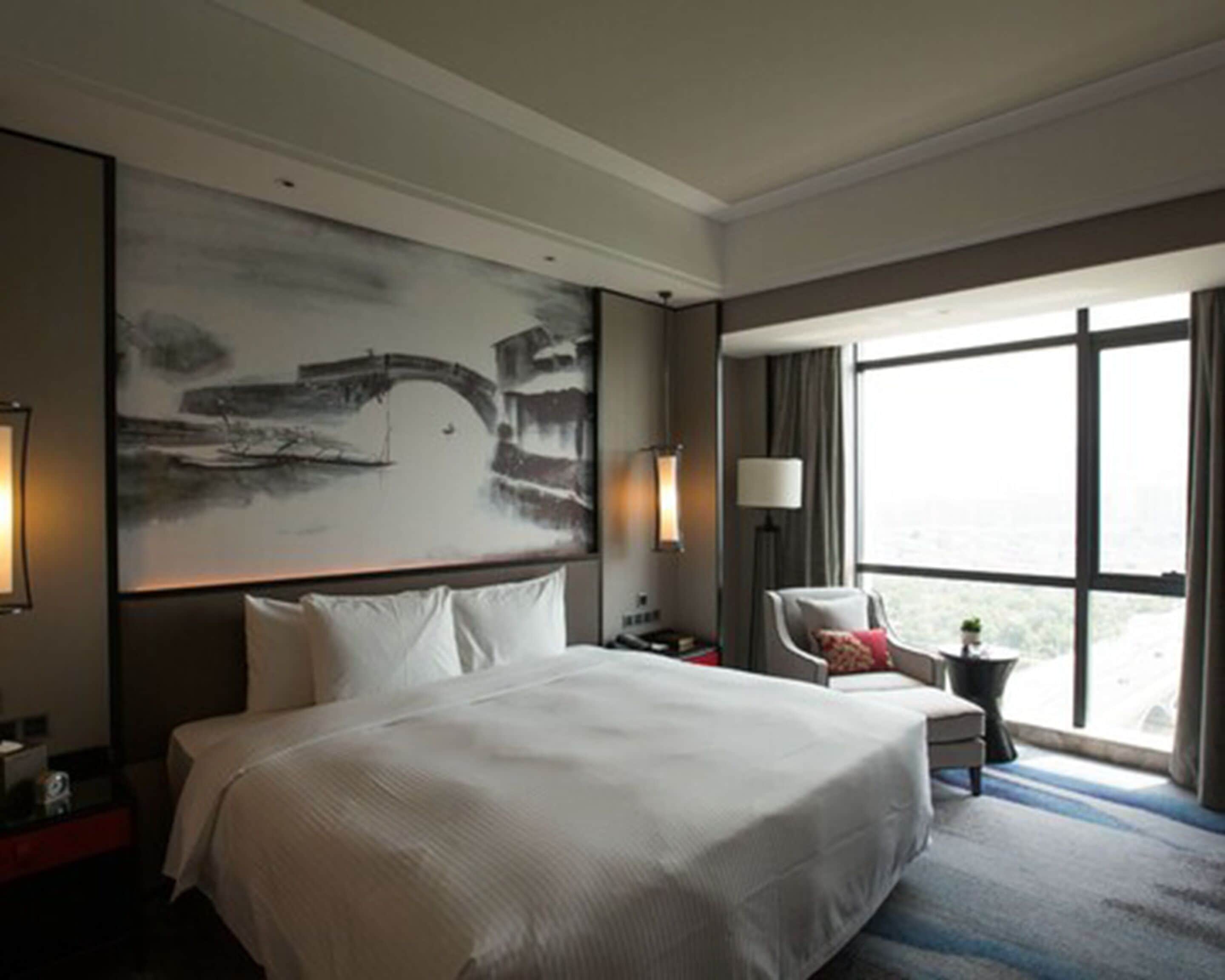 Een hotelkamer met een groot bed, een stoel, een bureau en een groot raam met uitzicht.