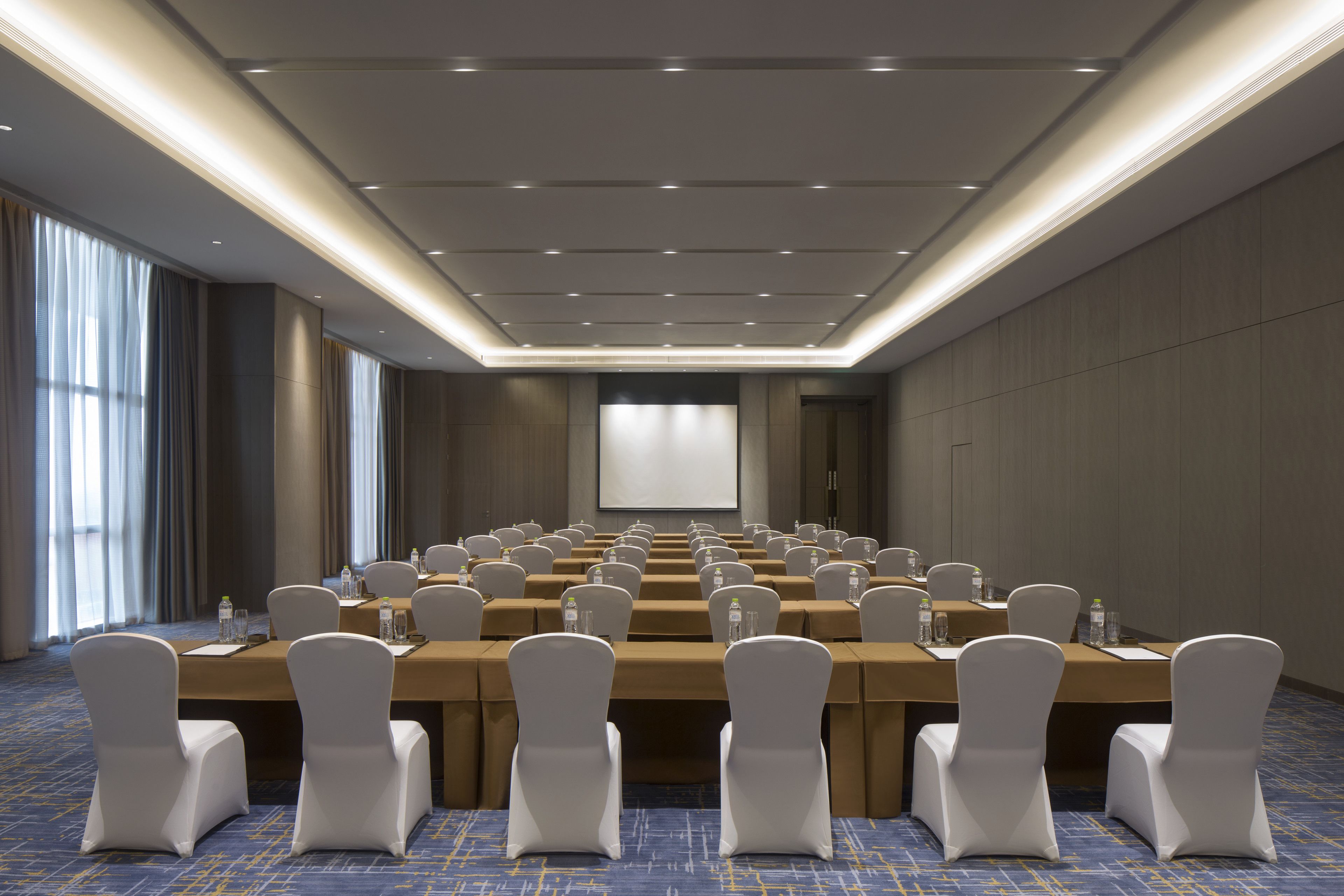 A conference room with multiple tables and chairs, equipped with water bottles and nameplates, in a modern hotel setting.