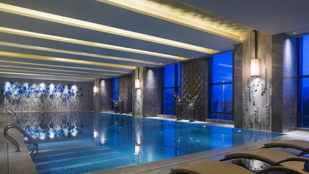 Una piscina interna moderna con acqua cristallina, sdraio e pannelli decorativi.