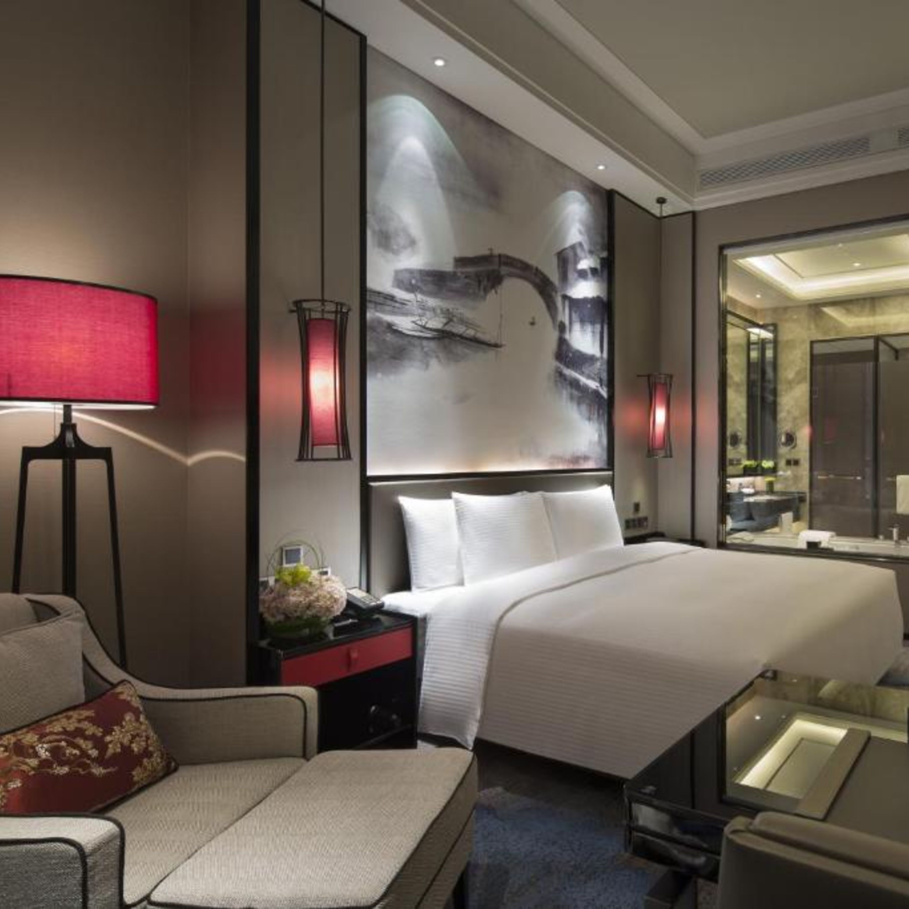 A modern hotel room with a large bed, a sofa, a desk, and a painting on the wall.