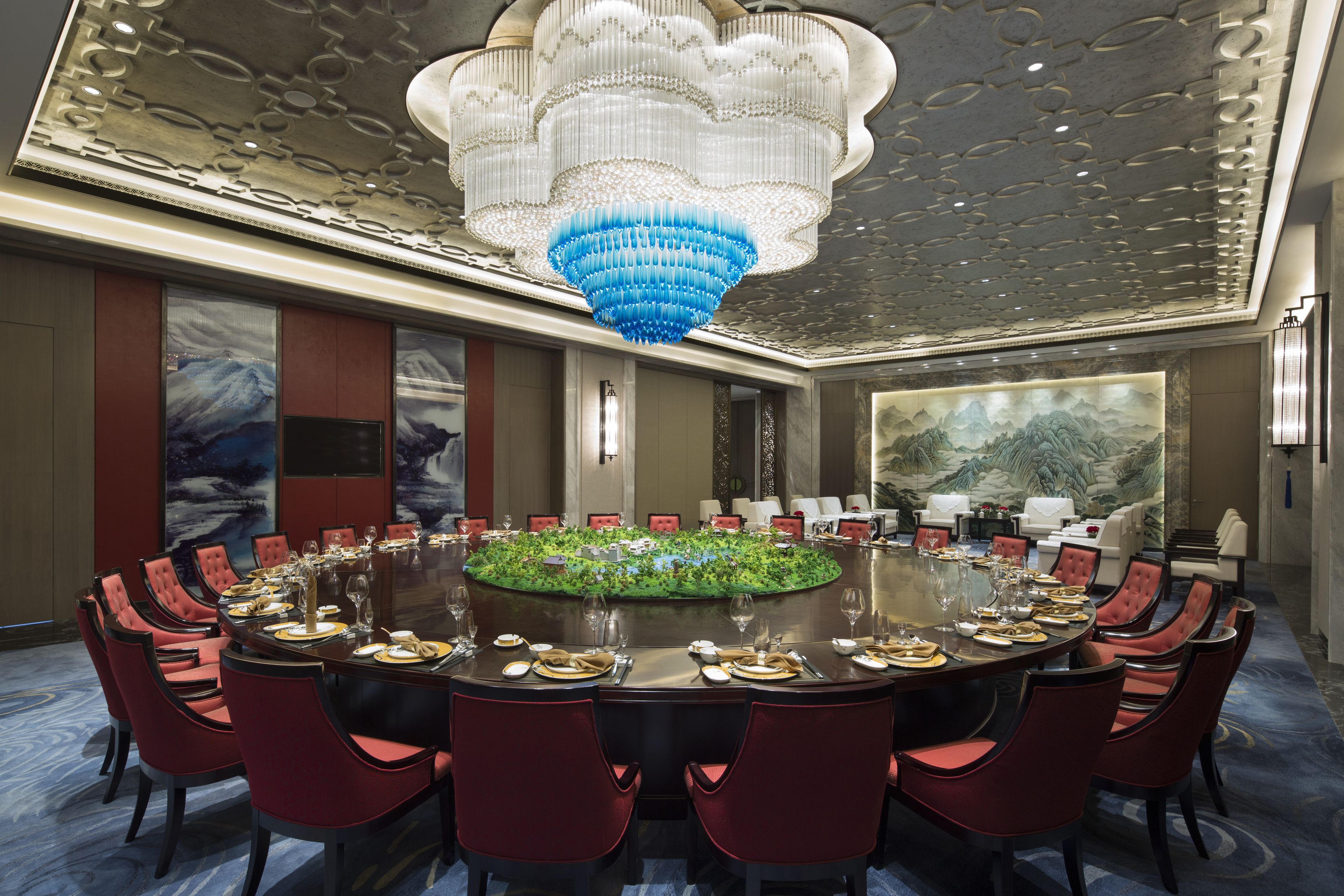A conference room with a round table, red chairs, and a chandelier.