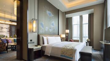 A modern hotel room with a large bed, bedside tables, a desk, and a seating area with a sofa and chairs.
