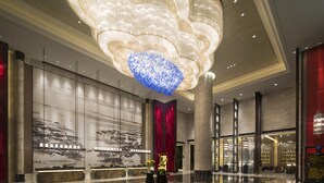 Un'ampia hall con un grande lampadario decorato, una reception e un muro con un dipinto tradizionale.