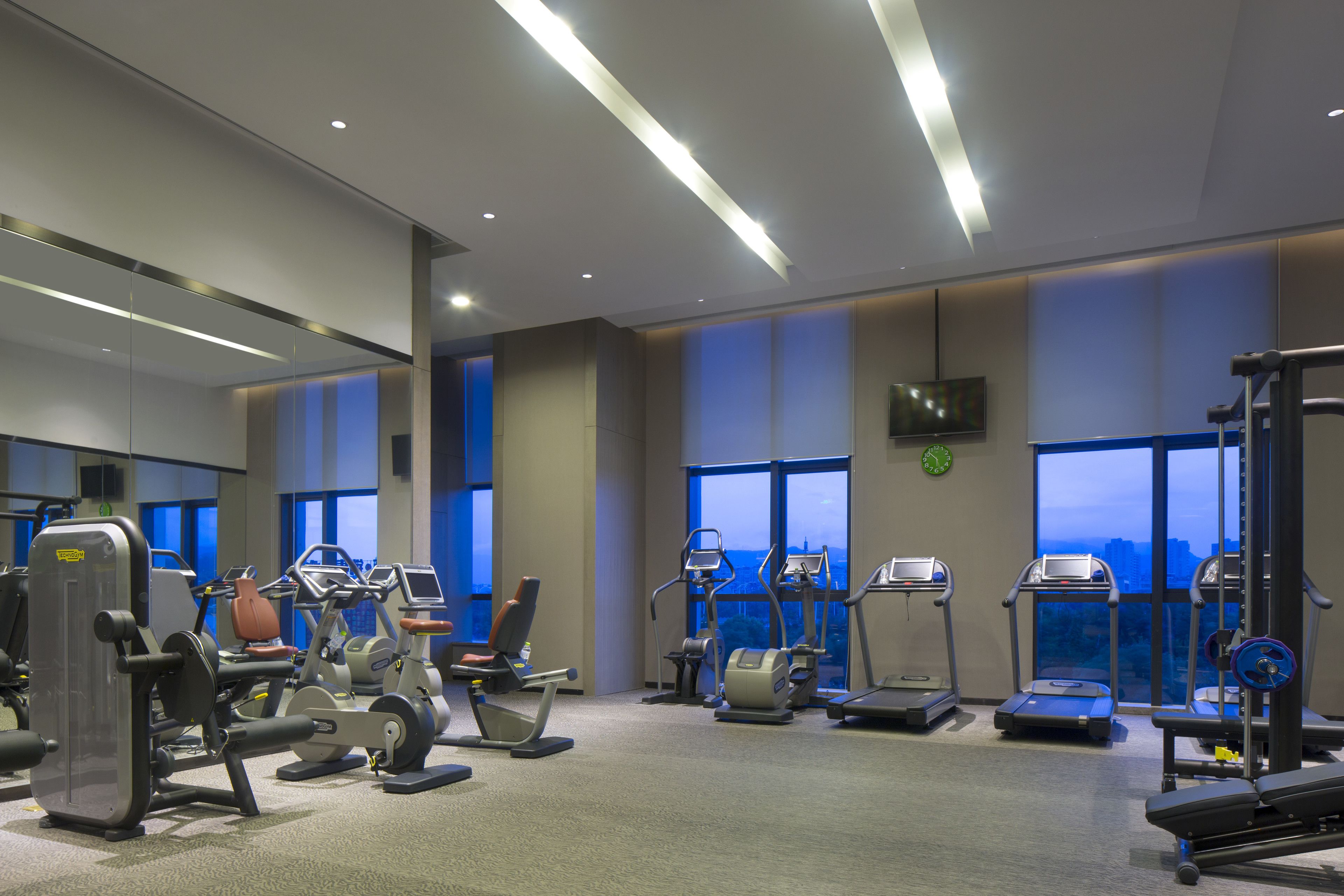Ein modernes Fitnessstudio mit unterschiedlichen Trainingsgeräten, großen Fenstern und Blick auf die Stadt.