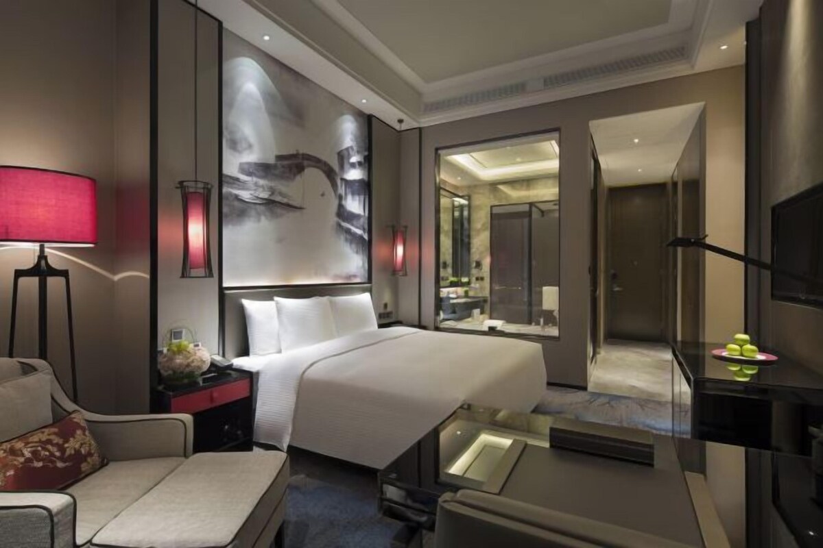 A modern hotel room with a large bed, a desk, a chair, a TV, and a mirror.