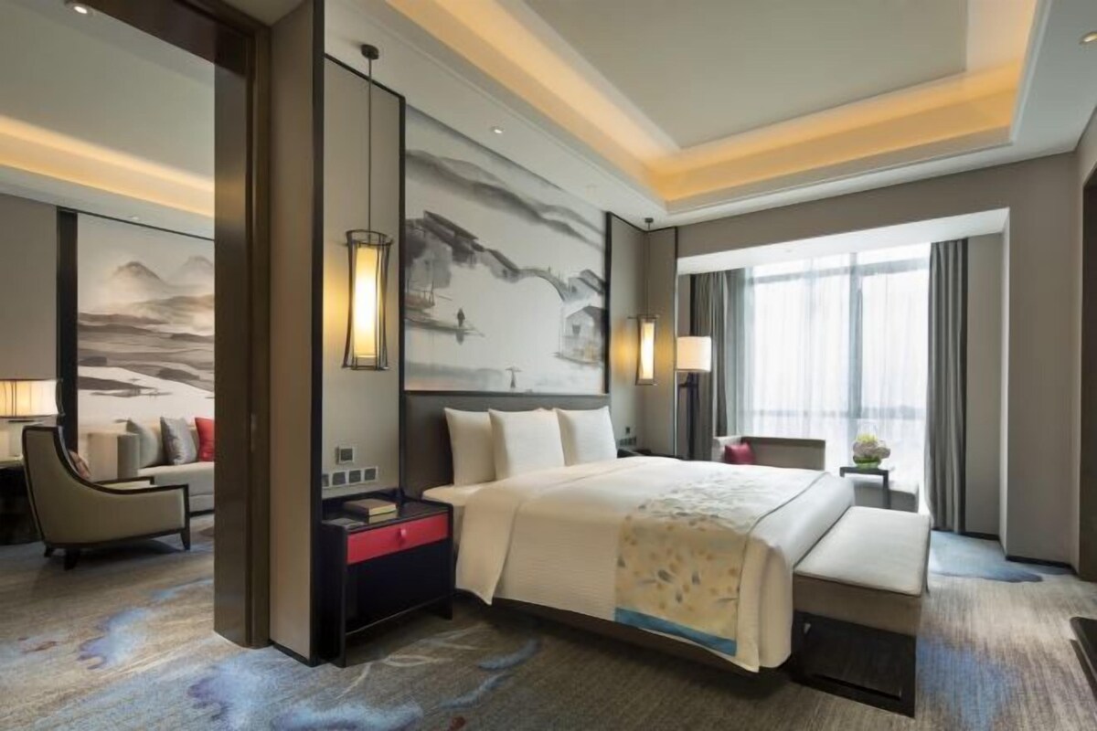 A hotel room with a large bed, a desk, a chair, and a painting on the wall.