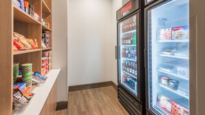 Un bar de aperitivos con estantes llenos de bocadillos y bebidas, y dos refrigeradores con un cartel de Coca-Cola Zero encima.